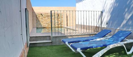 Un pequeño espacio al aire libre con piscina, dos sillones reclinables azules y una pequeña escalera que conduce a un muro de piedra.