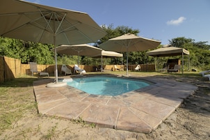 Um quintal com piscina, rodeado por ladrilhos de pedra e com grandes guarda-sóis.