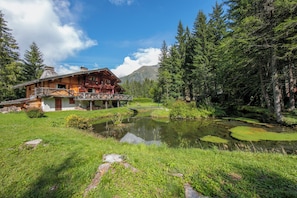 A wooden lodge with a pond, surrounded by forest and mountains.