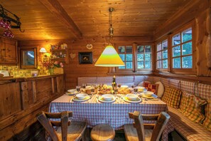 A wooden cabin interior with a dining table set for four, a sofa, and a large window.