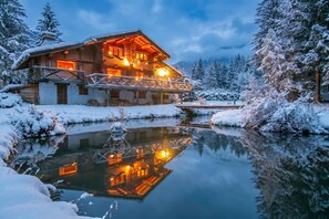 Een blokhut met een weerspiegeling in stil water, omringd door met sneeuw bedekte bomen.