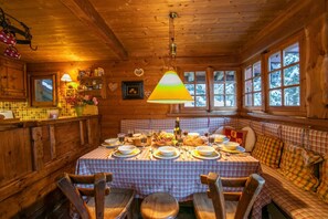 L’intérieur d’un chalet en bois présente une table à manger dressée pour quatre personnes, entourée de bancs et de chaises à motifs écossais.