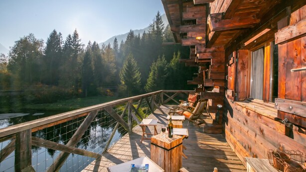 Een houten terras met buitenmeubilair, met uitzicht op een waterpartij en beboste bergen.