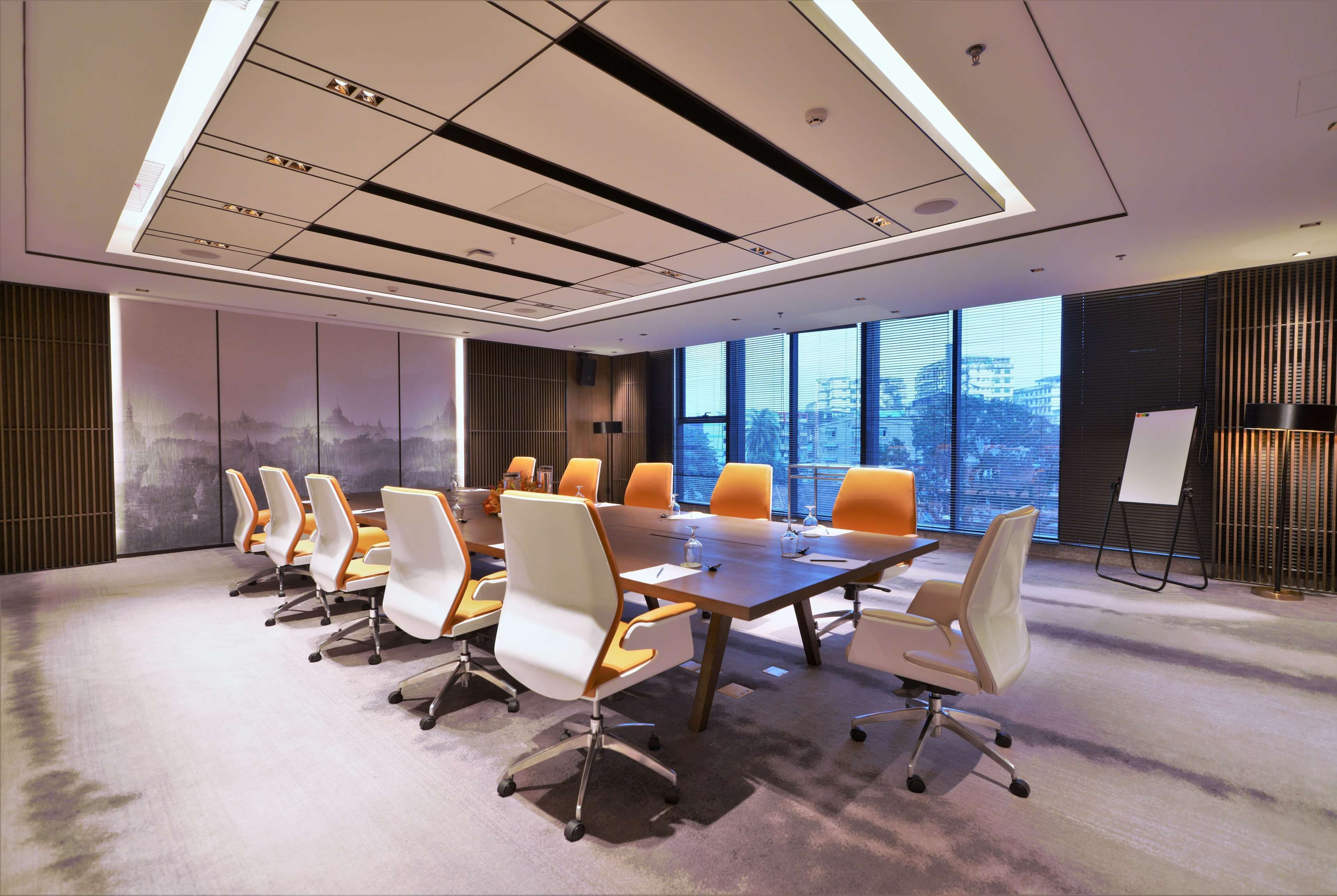 A conference room with a long table, multiple chairs, and large windows offering a city view.