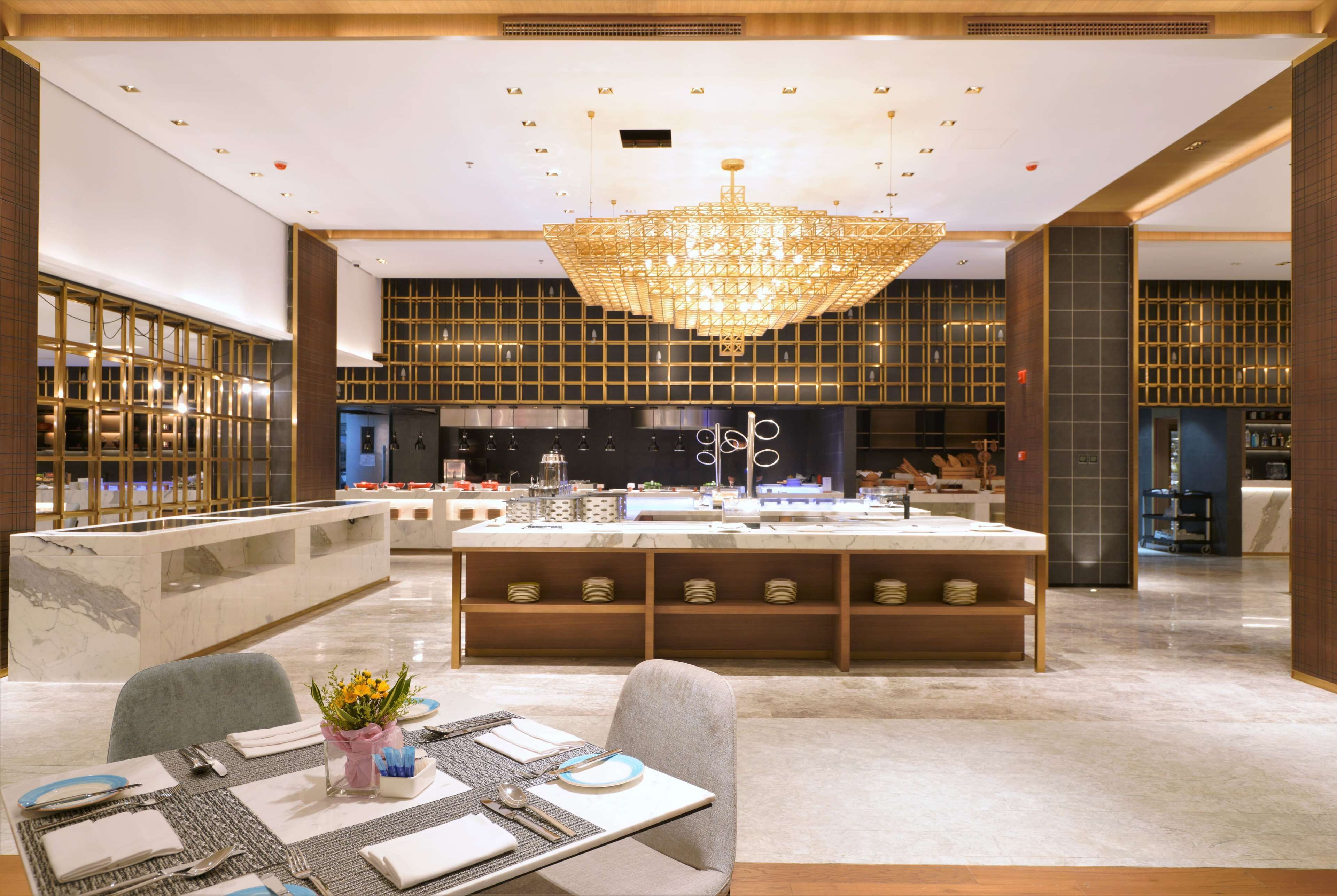 A modern hotel lobby with a central island, a chandelier, and a reception area.