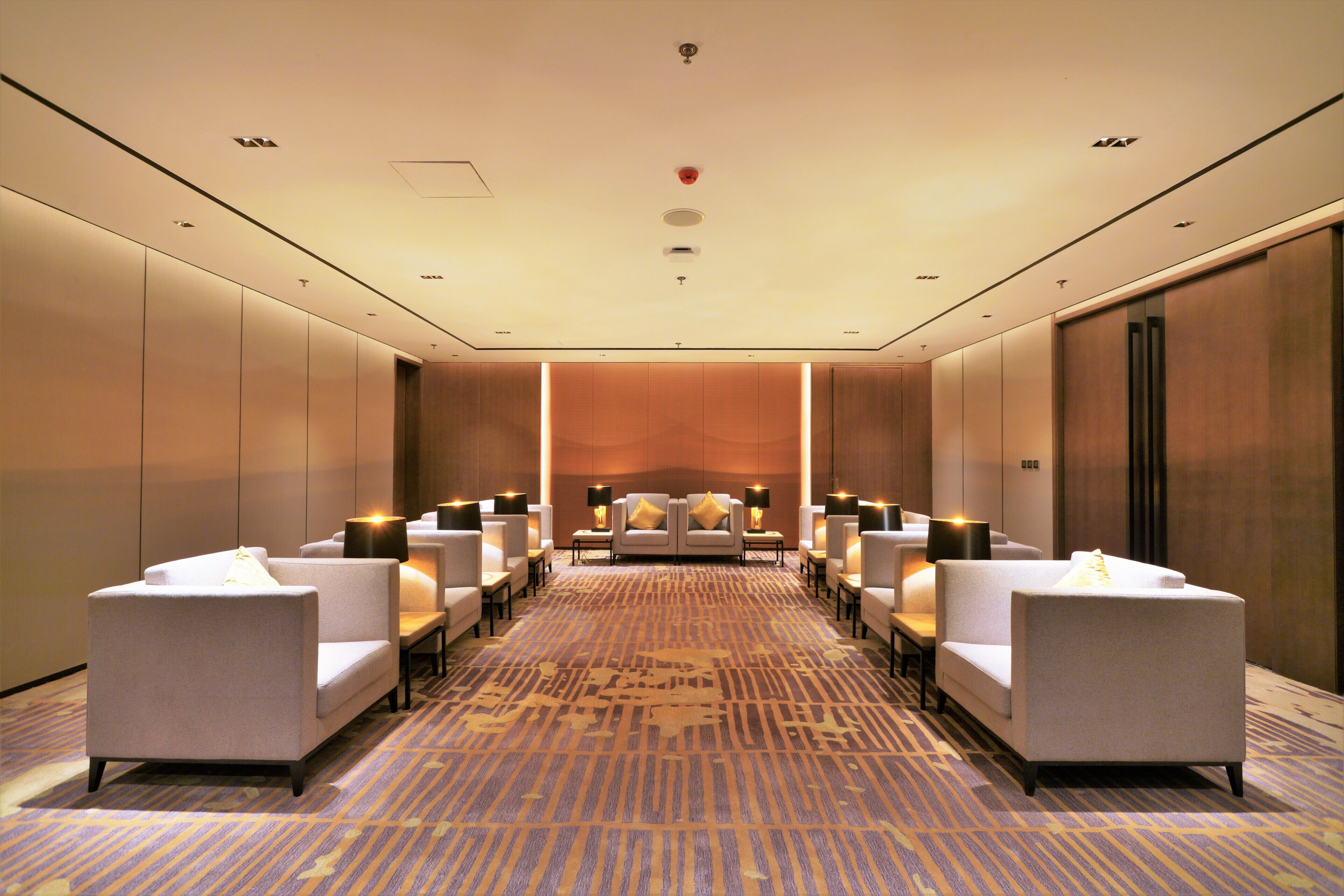 A hotel room with a long corridor, multiple seating areas, and a large bed at the end.