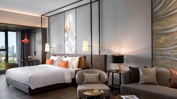 A modern hotel room with a large bed, a sofa, a chair, a small table, and a view of the city.