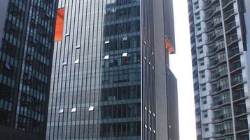 Un moderno edificio de gran altura con ventanas de vidrio reflectante y una señalización naranja visible.
