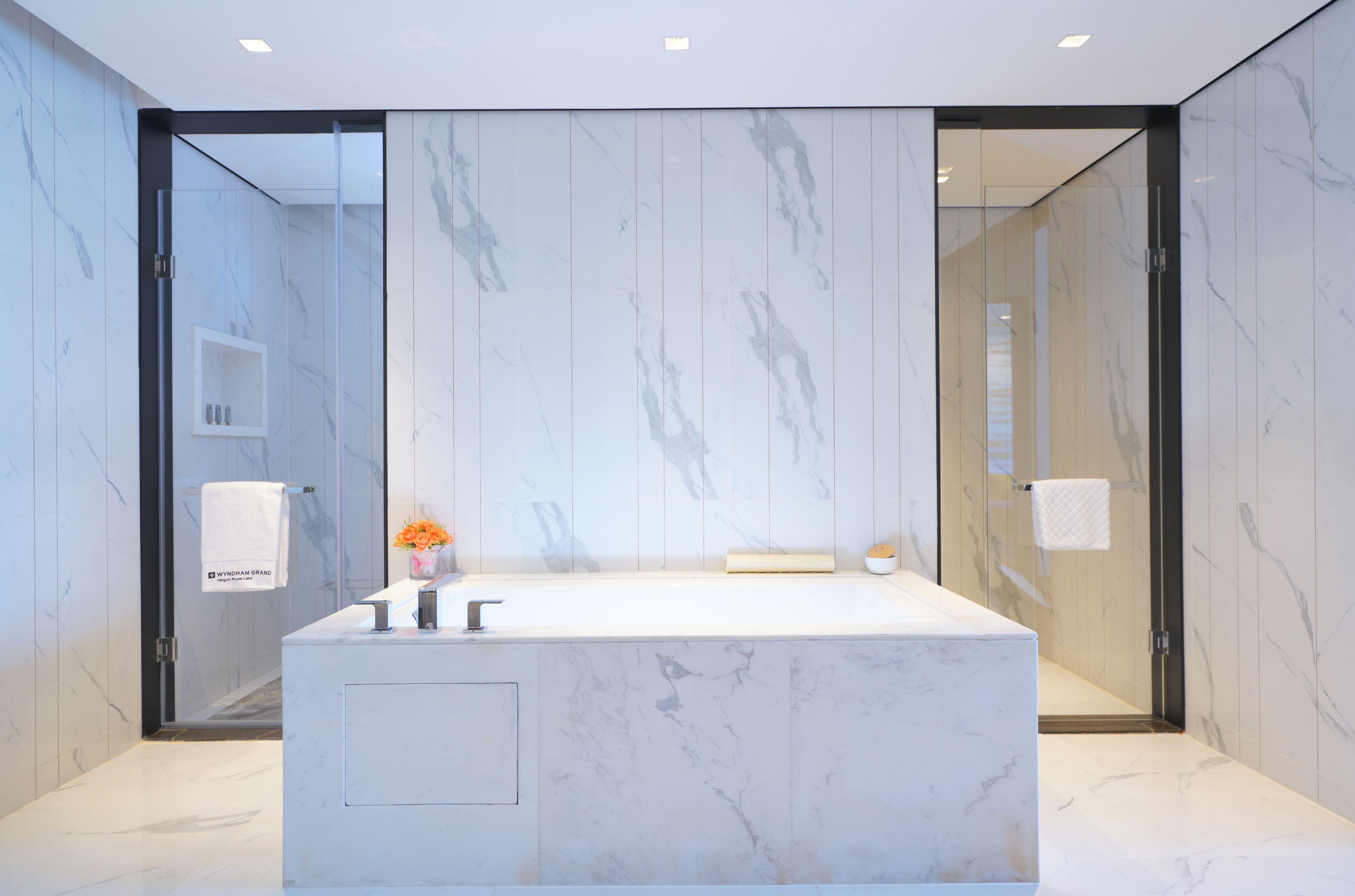A modern bathroom with a large marble sink, glass shower enclosure, and marble walls.