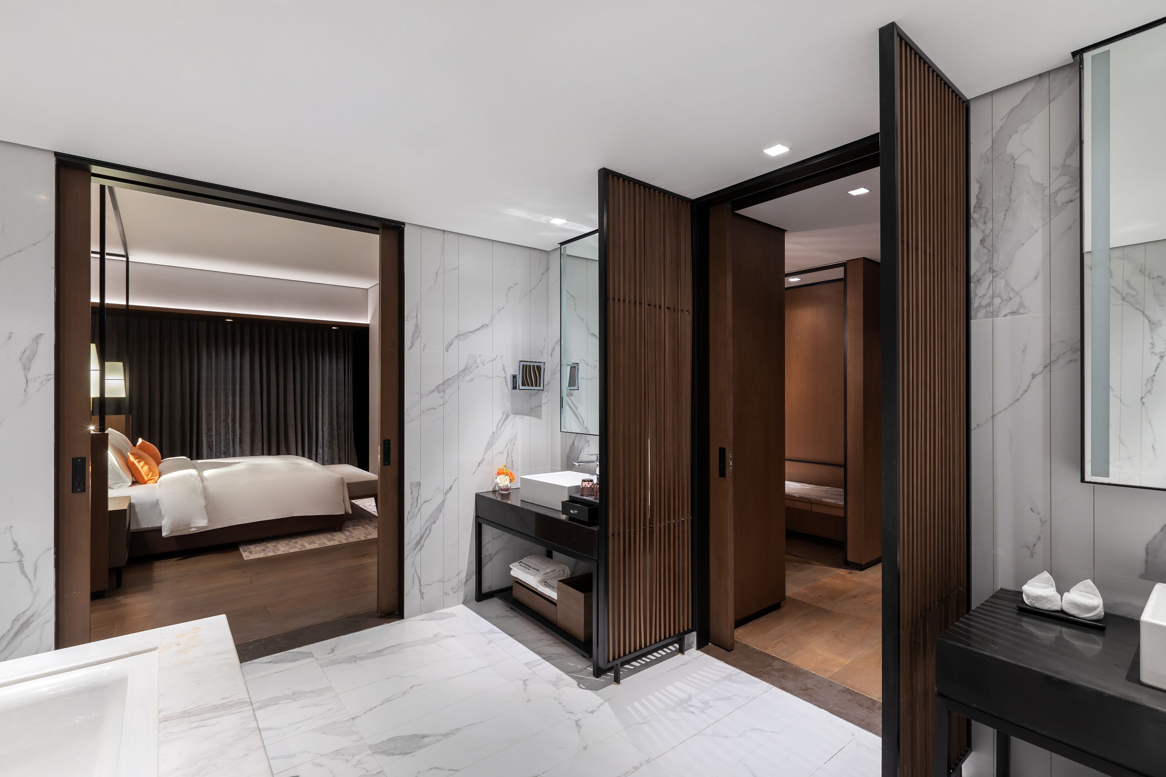 A modern hotel room with a large bed, a vanity with a mirror, and a separate bathroom area.
