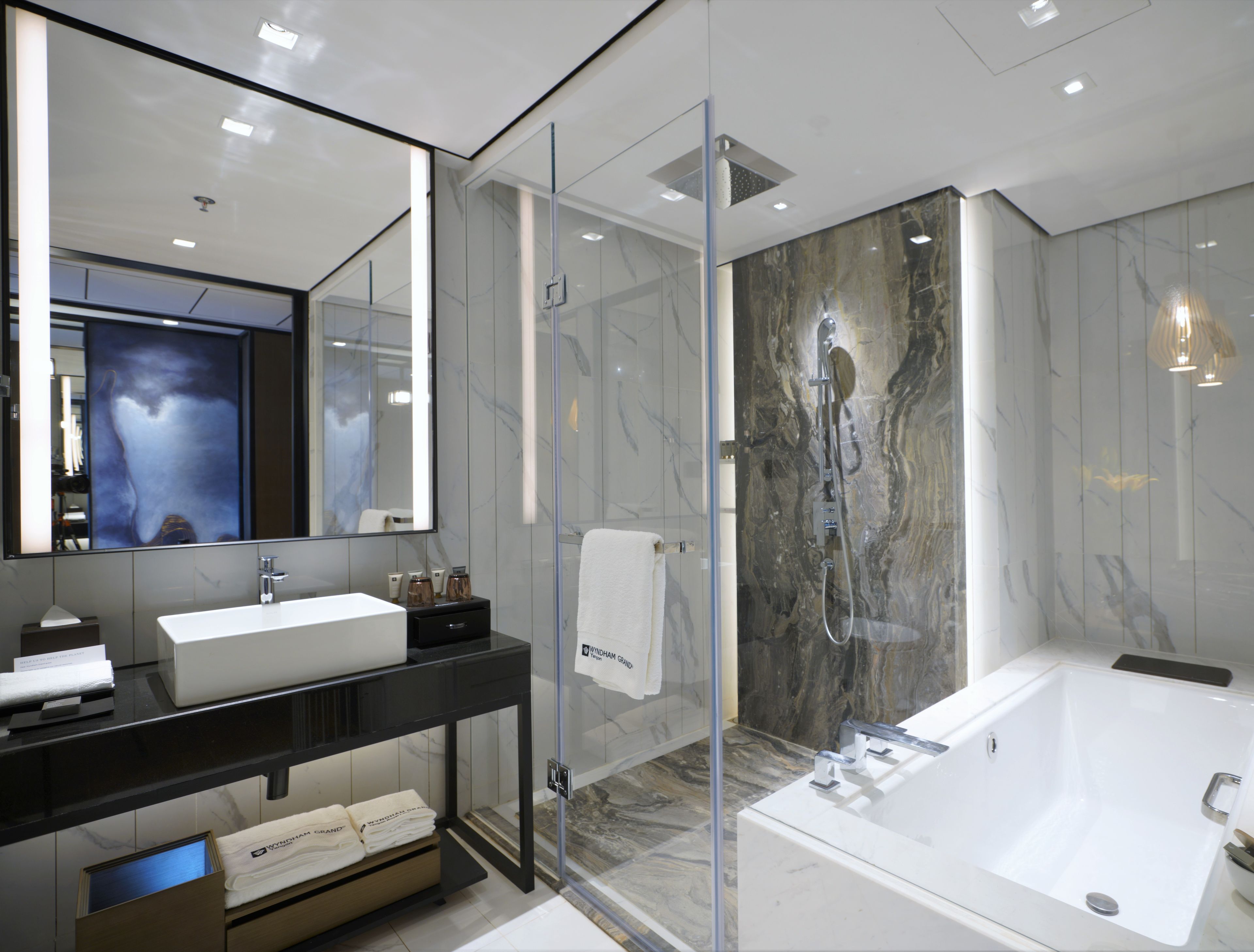 A modern bathroom with a large mirror, a white sink, a black vanity, a glass shower enclosure, and a white bathtub.