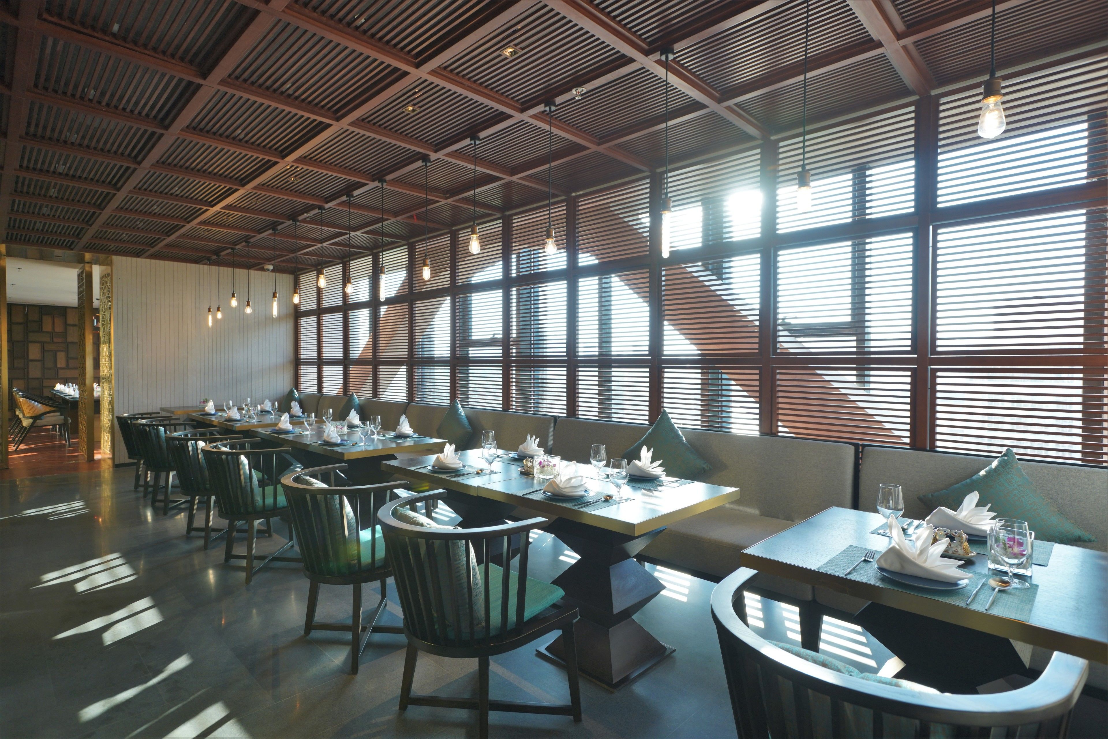 Een eetruimte met meerdere gedekte tafels, met een modern industrieel plafondontwerp en grote ramen voor natuurlijk licht.