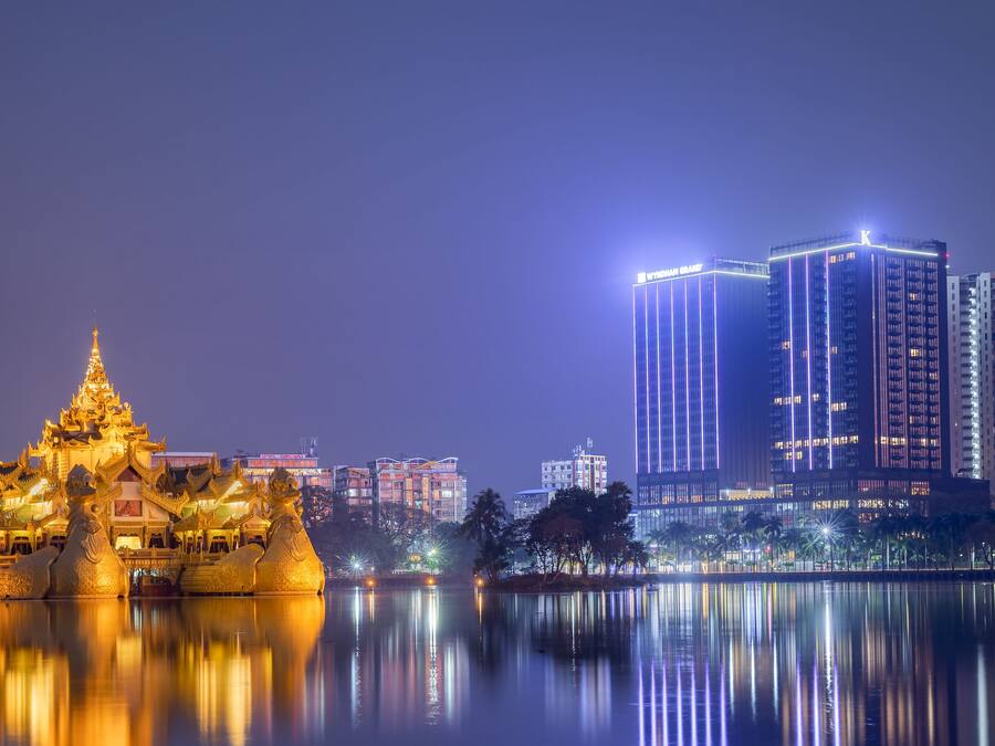 A nighttime view of a traditional temple with a reflection in the water, adjacent to modern high-rise buildings.