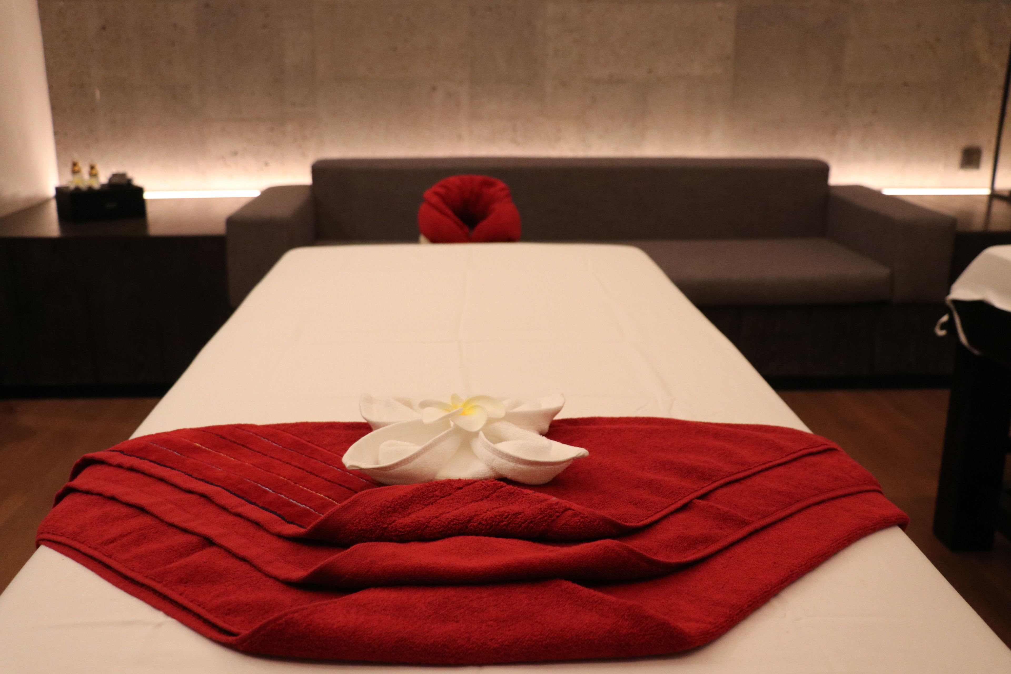 Une salle de spa équipée d’une table de massage, de serviettes rouges et d’une fleur blanche.