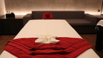 A spa room with a massage table, red towels, and a white flower.