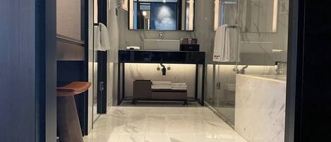 A modern bathroom with a marble floor, a black vanity, a glass shower enclosure, and a large mirror above the sink.