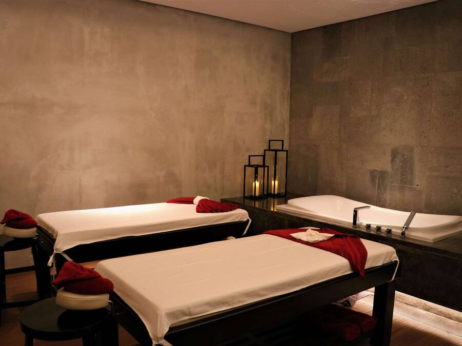 A spa room with two beds, a large mirror, and a bathtub.
