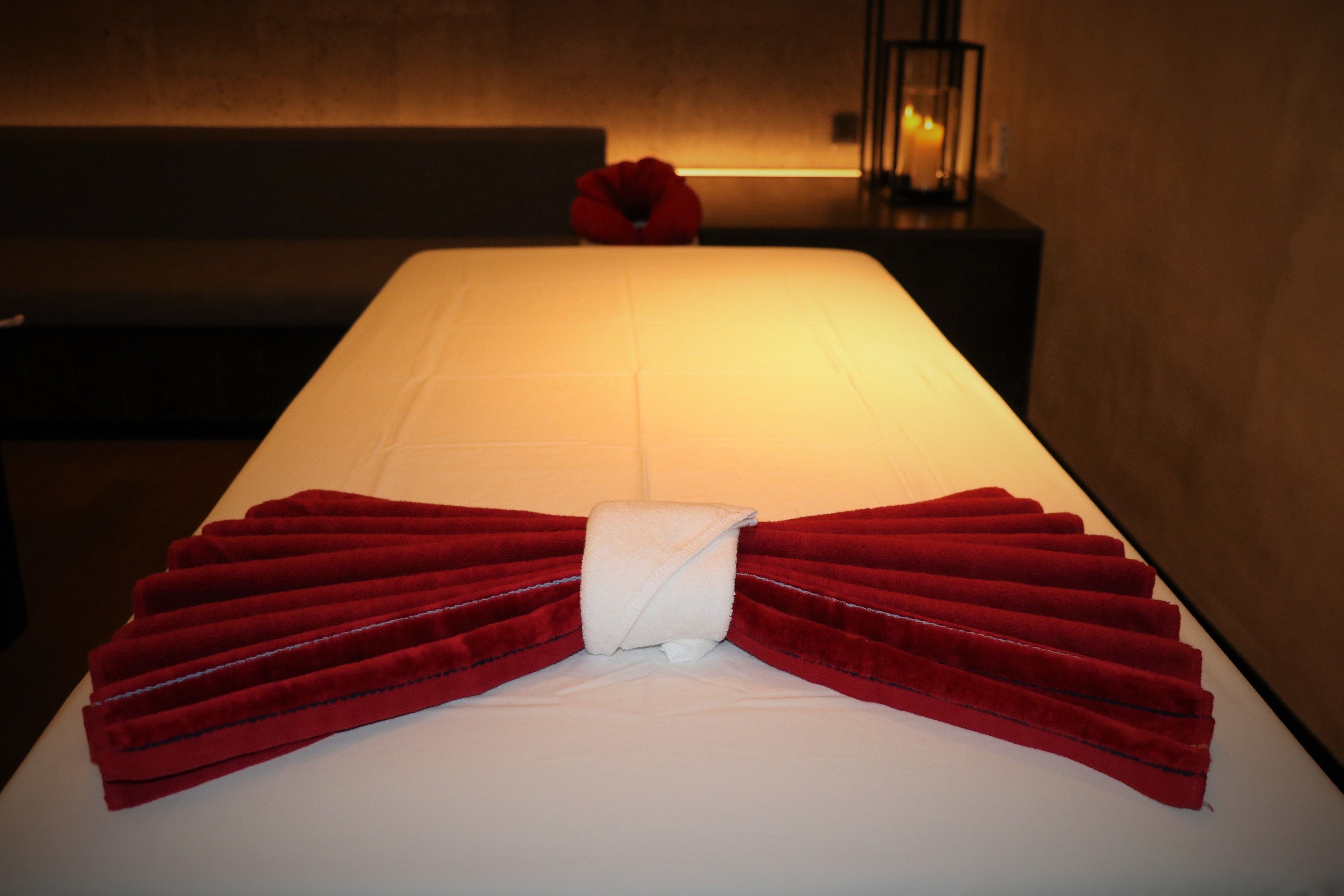 A neatly made bed with a red towel arrangement and a white pillow.