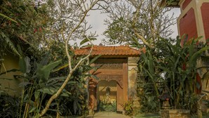 A garden pathway leading to a traditional building with a tiled roof and ornate doorway. - Villa Chempaka (Ubud)