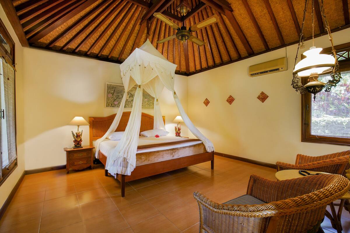 A bedroom with a four-poster bed, a wooden ceiling, and wicker furniture.