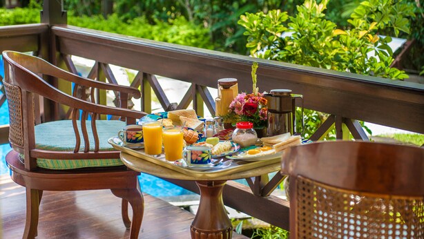 A wooden deck with a breakfast tray, a chair, and a table. - Villa Chempaka (Ubud)