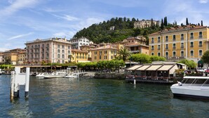 Eine Uferpromenade mit Stadtbild, historischen Gebäuden, einem Yachthafen und einem Hügel mit einer schlossartigen Struktur.
