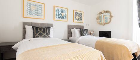A hotel room with two beds, a fireplace, and three framed artworks on the wall.