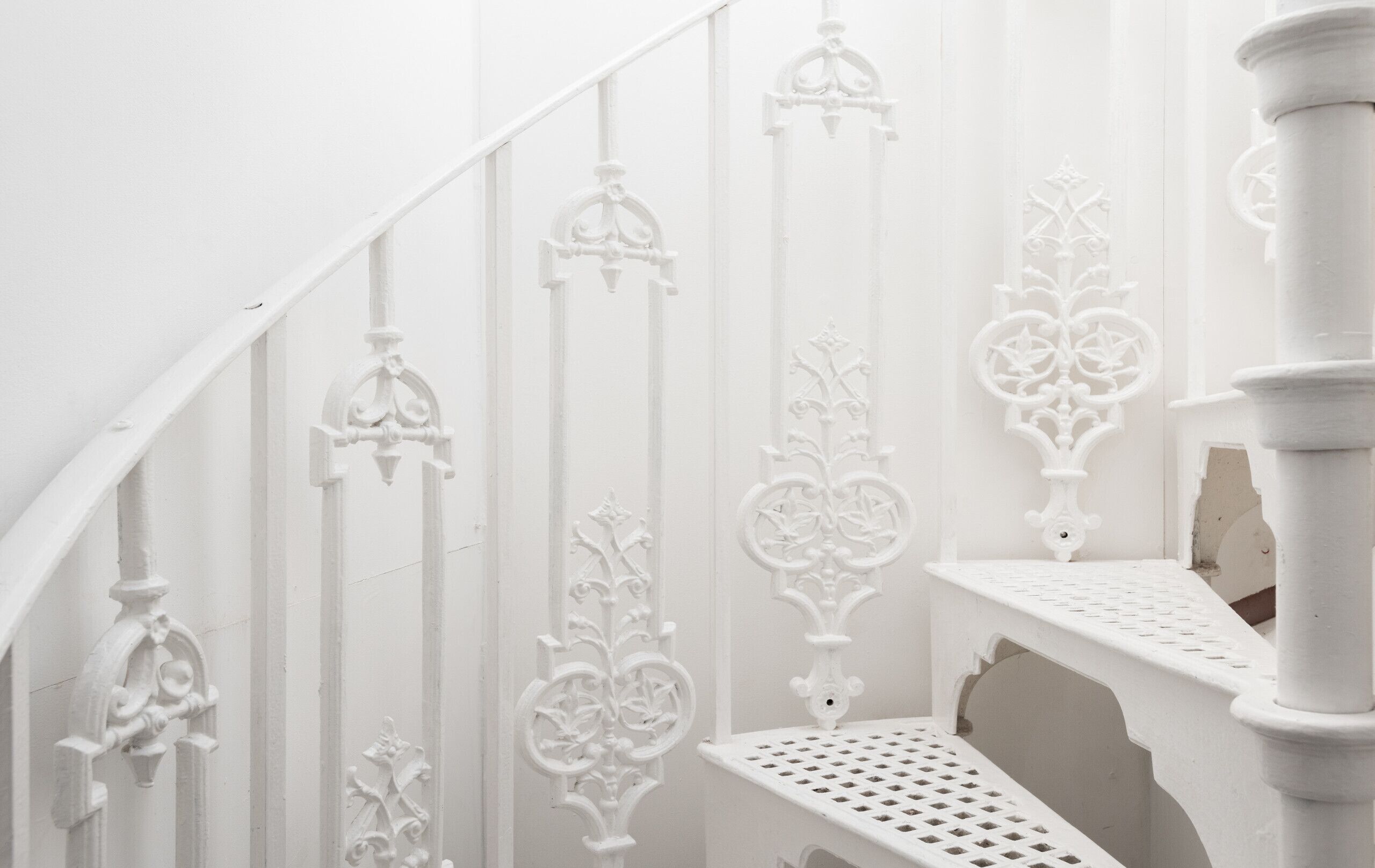 A white staircase with ornate metal railings and a white bench.