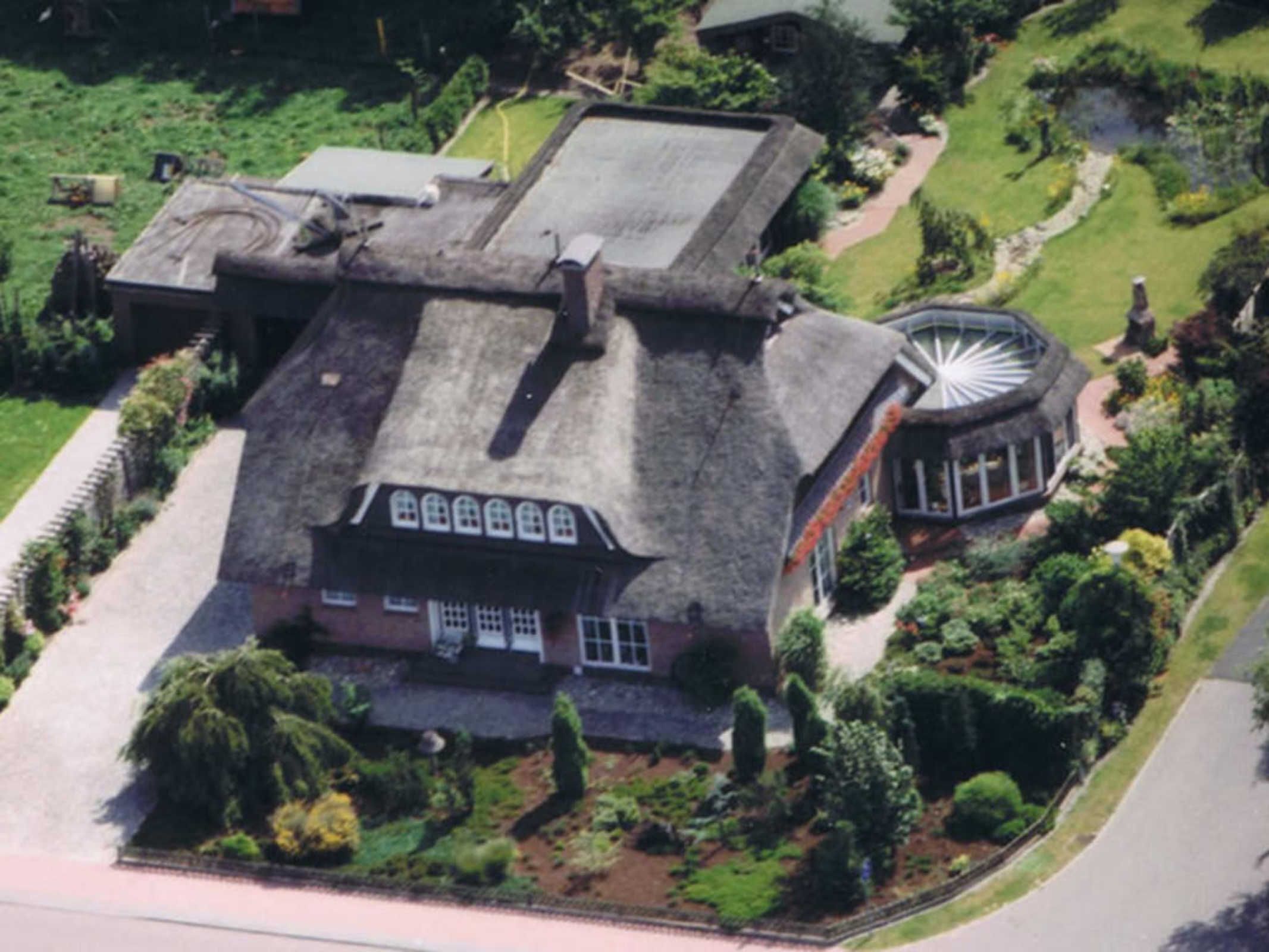 Vista aérea de una casa grande e histórica con una torre circular destacada, rodeada de jardines cuidados y un camino pavimentado.