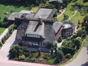 An aerial view of a large, historic house with a prominent circular tower, surrounded by well-maintained gardens and a paved driveway. - Ferienwohnung Peters Am Kanal 35606 - Holiday apartment Am Kanal, 35606 (Uplengen)