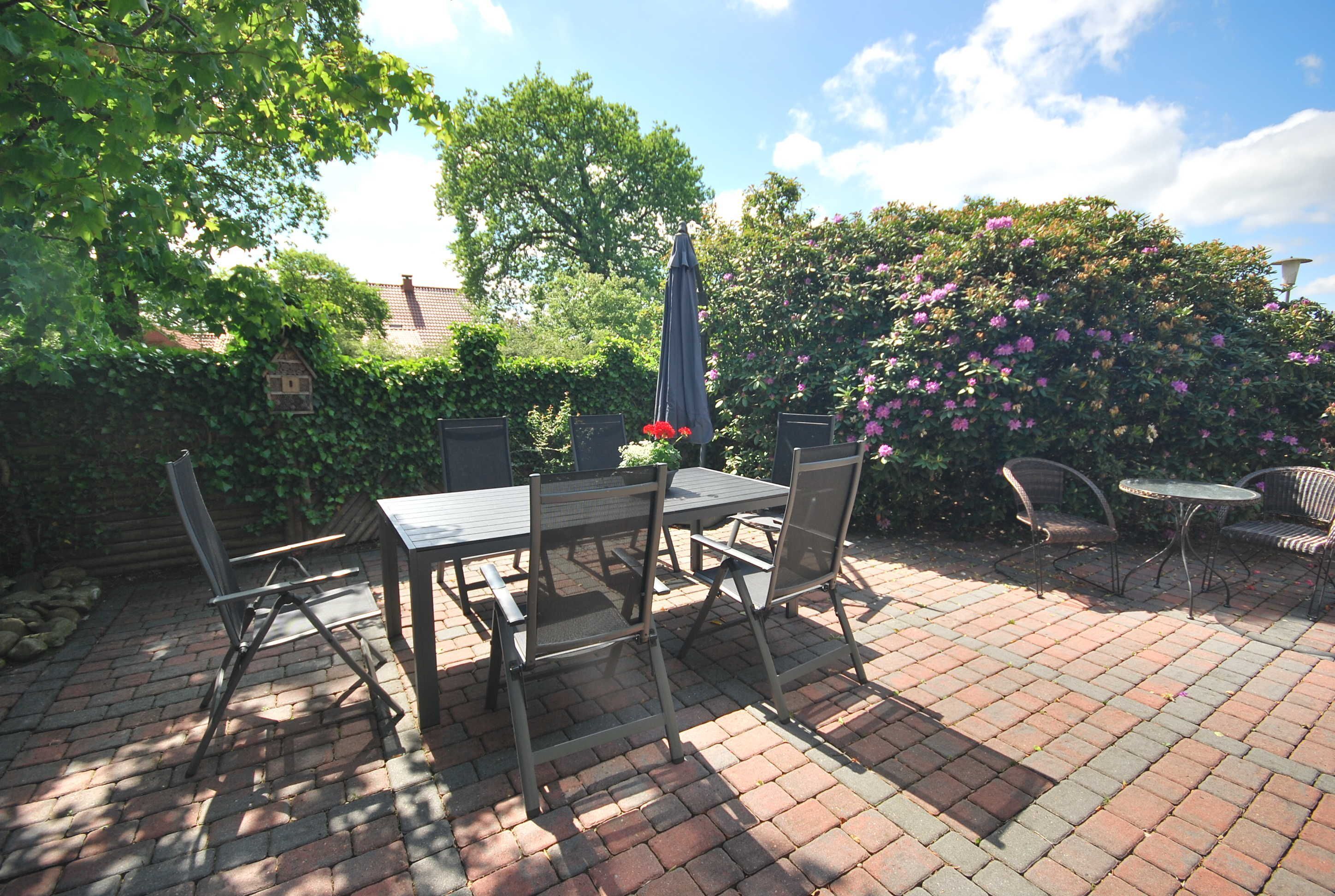 An outdoor patio with a brick floor, a table with chairs, and a small garden area with a birdhouse and flowering plants.