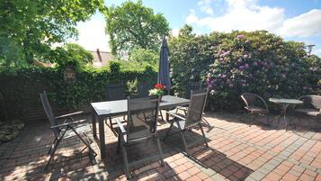 An outdoor patio with a brick floor, a table with chairs, and a small garden area with a birdhouse and flowering plants.