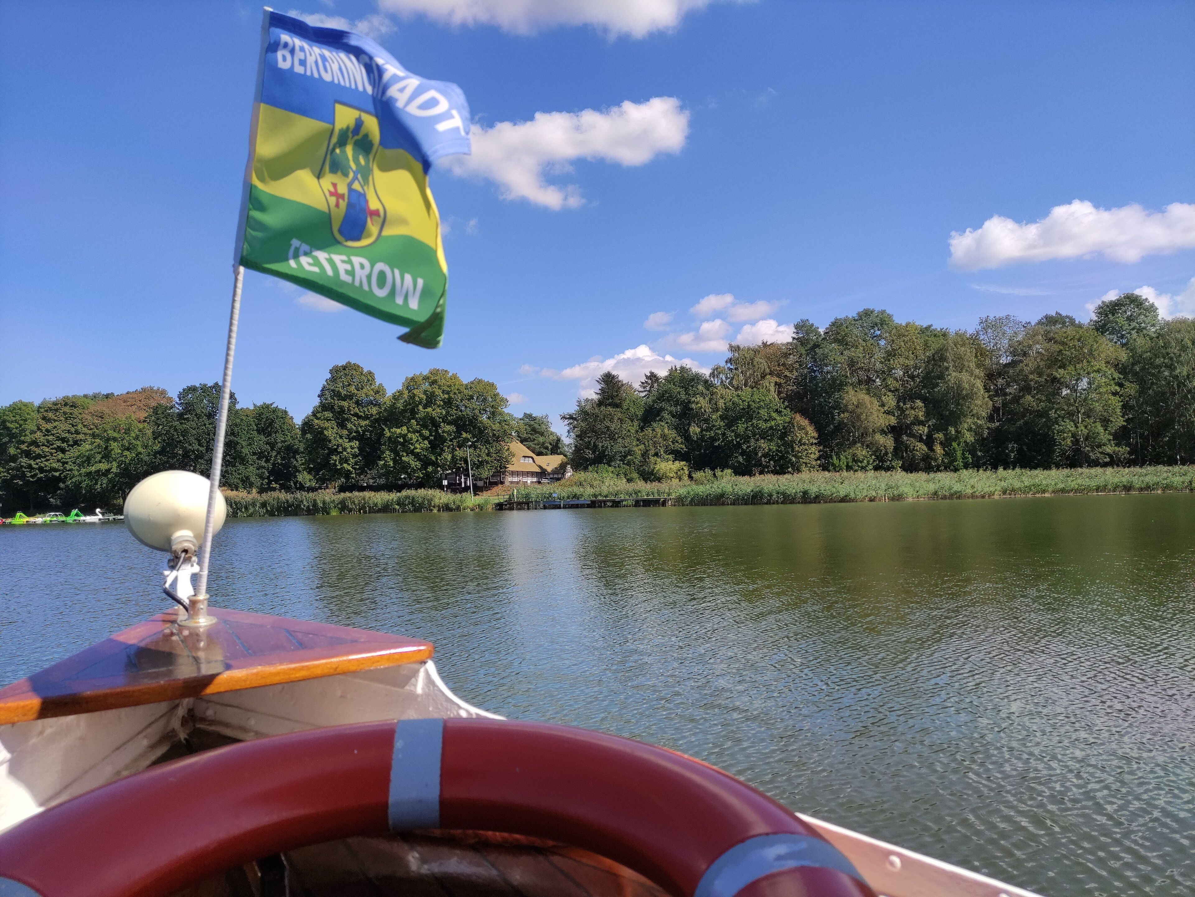 A boat with a flag, a lifebuoy, and a calm lake with trees in the background.