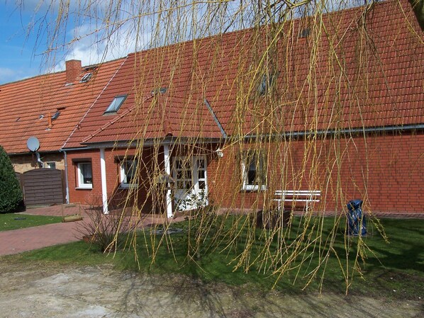 Une maison en briques rouges, avec un toit en pente, un petit porche et une antenne parabolique bien visible.