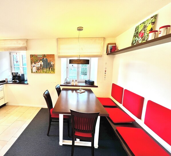 A dining area with a wooden table, red upholstered benches, and a painting on the wall.
