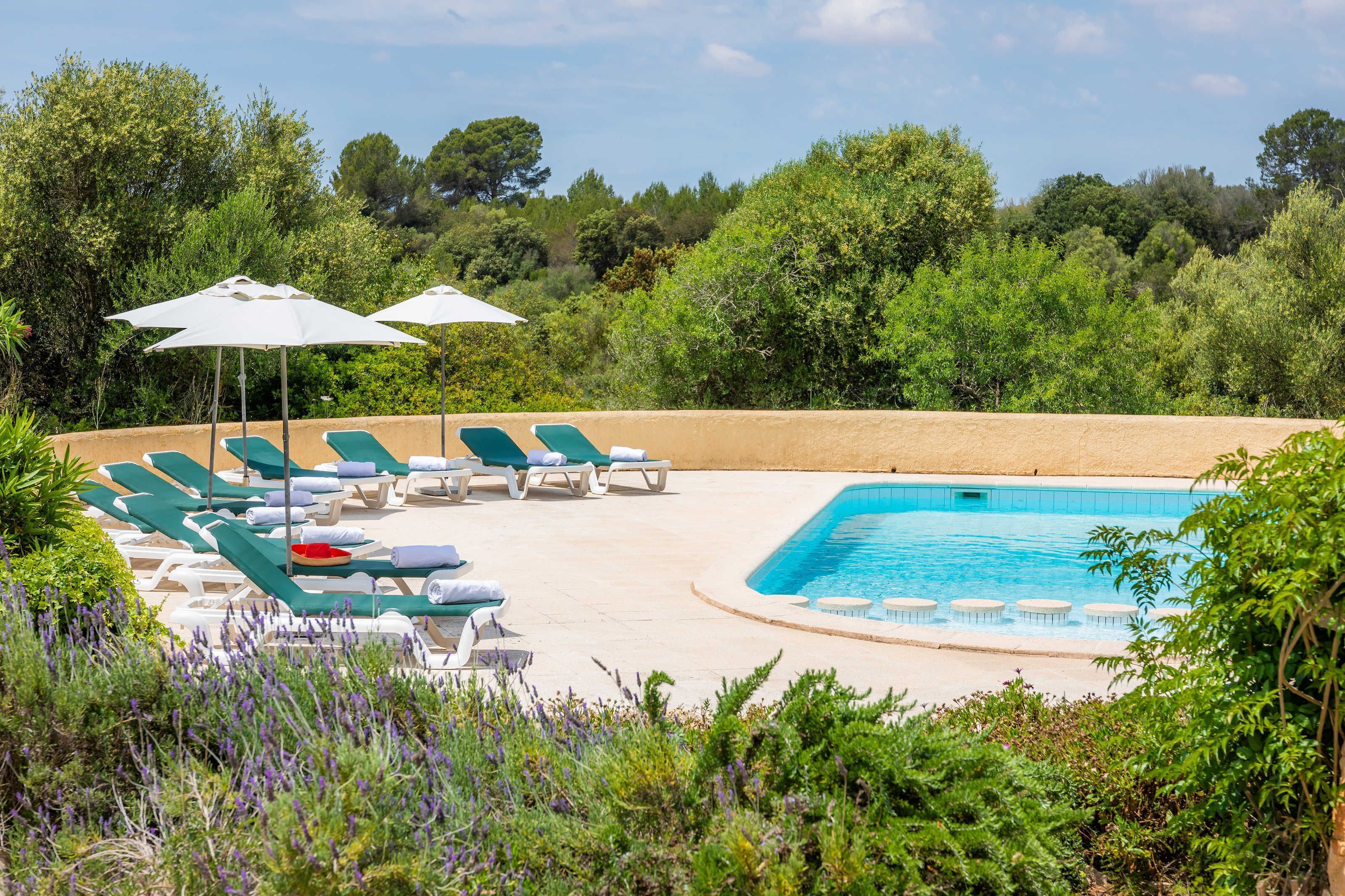 A pool area with lounge chairs and umbrellas, surrounded by greenery.