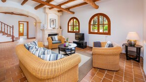A living room with wicker furniture, a fireplace, a television, and large arched windows.