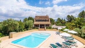 A pool with lounge chairs and umbrellas, a building with arches, and a landscaped garden.