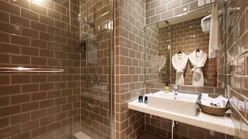 A modern bathroom with a glass-enclosed shower, a white sink, and a mirror reflecting two white robes.