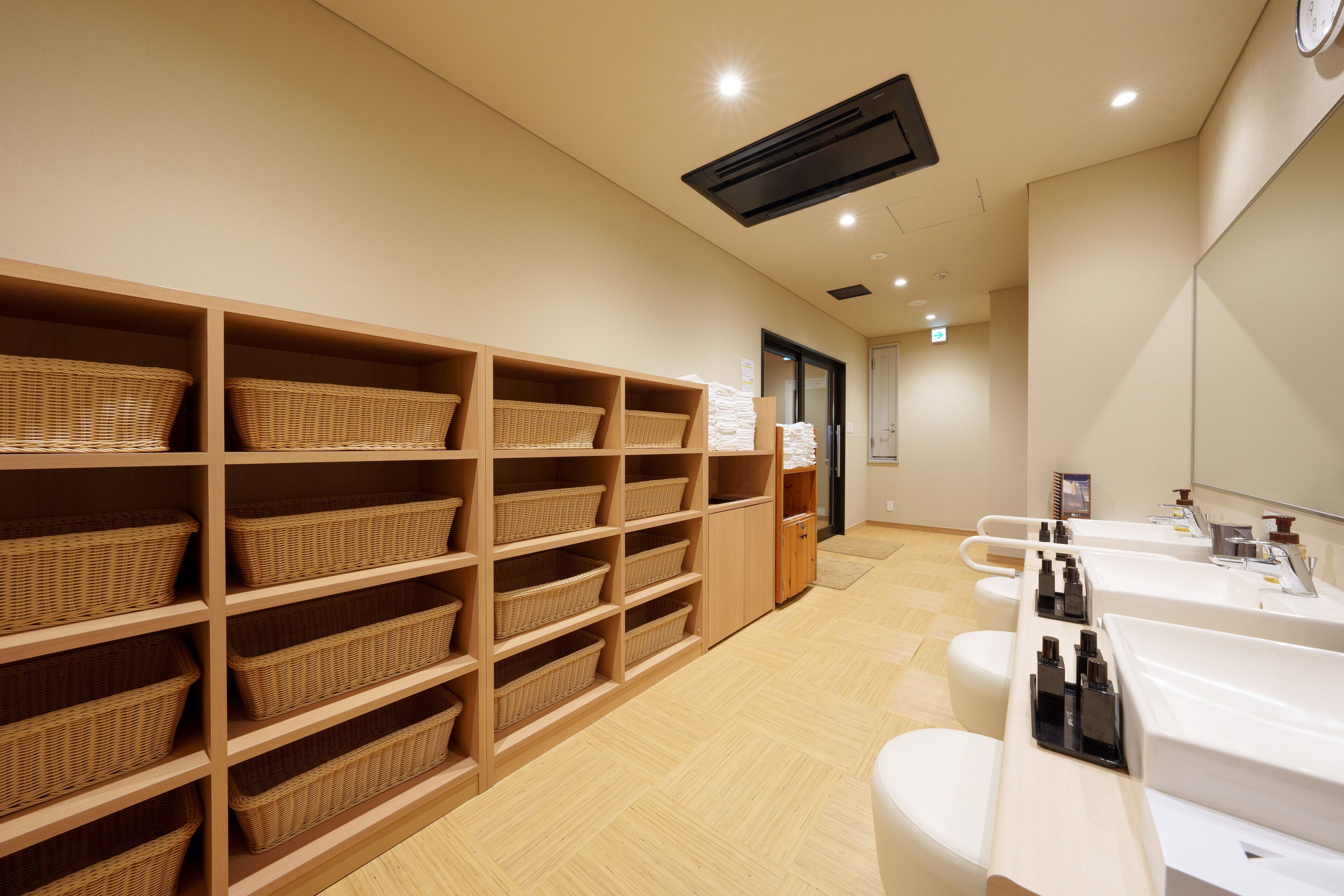 A clean, modern bathroom with multiple sinks, wicker baskets on shelves, and a wooden floor.