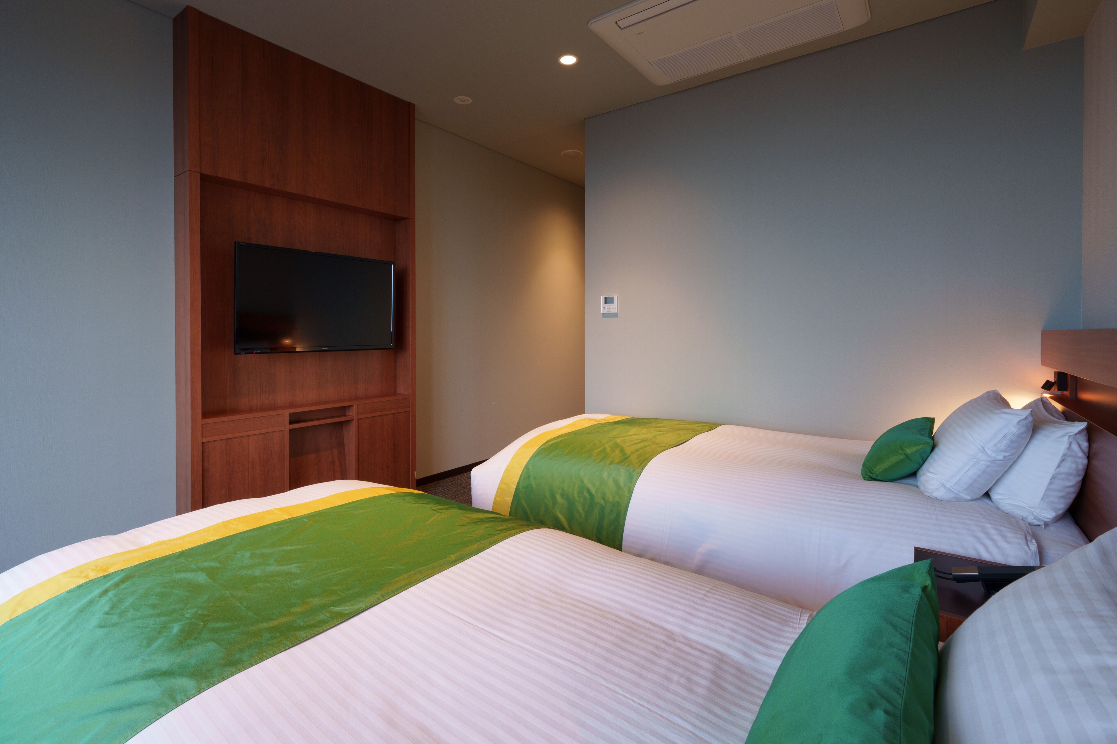 A hotel room with two beds, a flat-screen TV mounted on the wall, and a wooden cabinet.