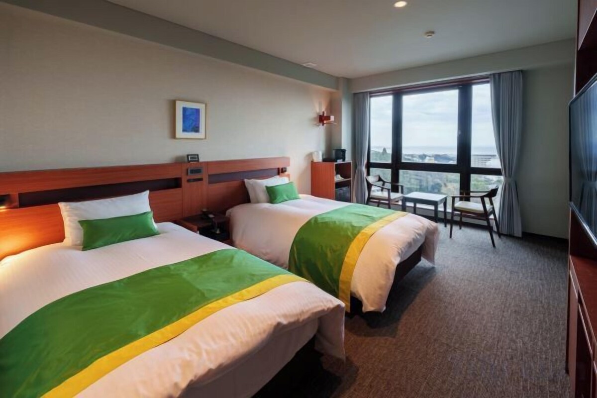A hotel room with two beds, a desk, and a large window.