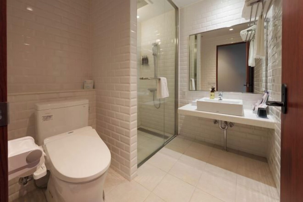A modern bathroom with a toilet, a glass-enclosed shower, and a sink with a mirror above it.
