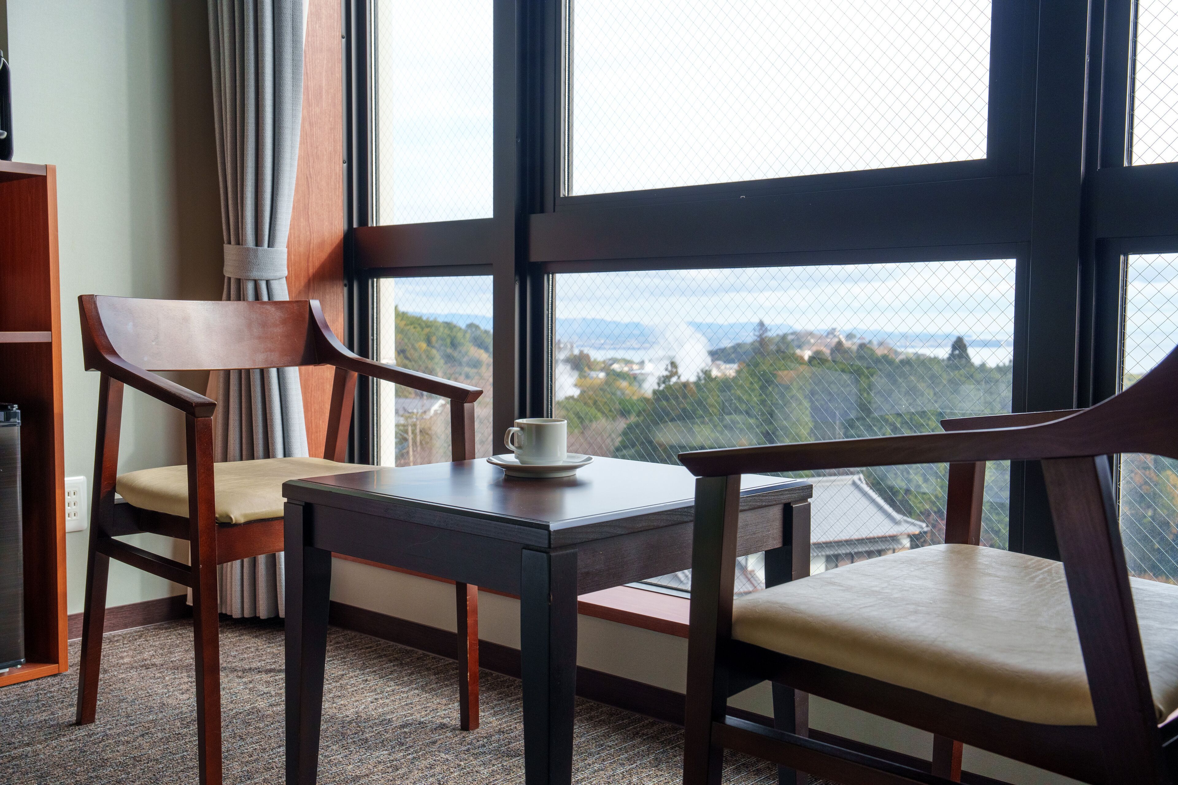 A room with two wooden chairs, a small table, and a window offering a view of a mountainous landscape.