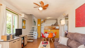 Uma sala de estar com sofá, mesa de centro, televisão e uma área de jantar com cadeiras e mesa.