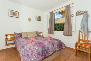 Ein Schlafzimmer mit Bett, Sessel, Fenster mit Vorhängen und zwei an der Wand hängenden Bildern.