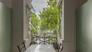 Un balcón con mesa y sillas, rodeado de follaje y vistas a un parque.