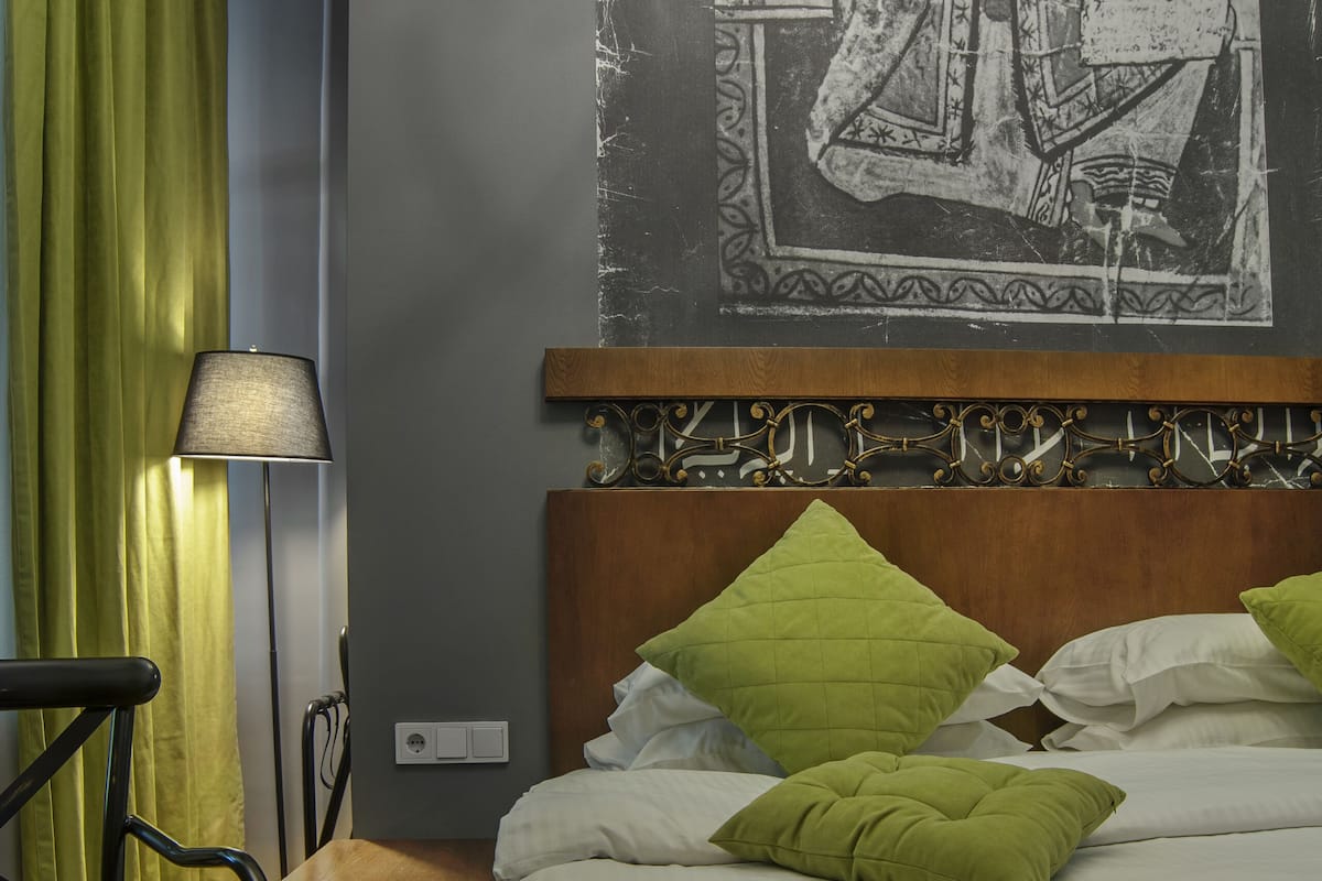 Een netjes opgemaakt bed met groene beddengoed, een nachtkastje met een lamp en een aan de muur bevestigd kunstwerk.