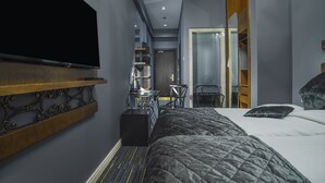 Una habitación de hotel con cama, televisión montada en la pared, escritorio con silla y armario.