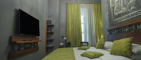 Una habitación de hotel con cama, televisión de pantalla plana, escritorio con lámpara y un cuadro en la pared.